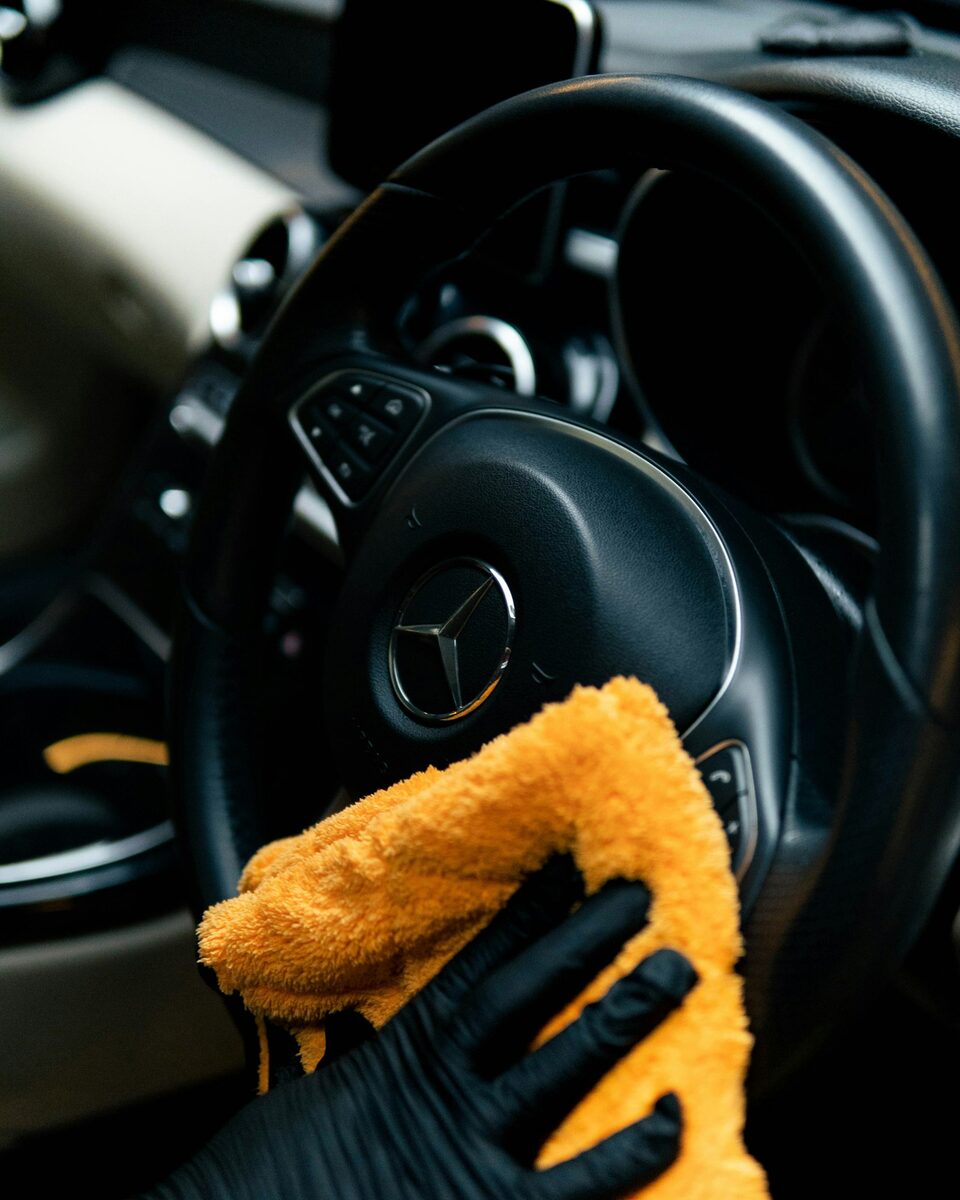 Gloved hand wiping a car steering wheel with a microfibre cloth