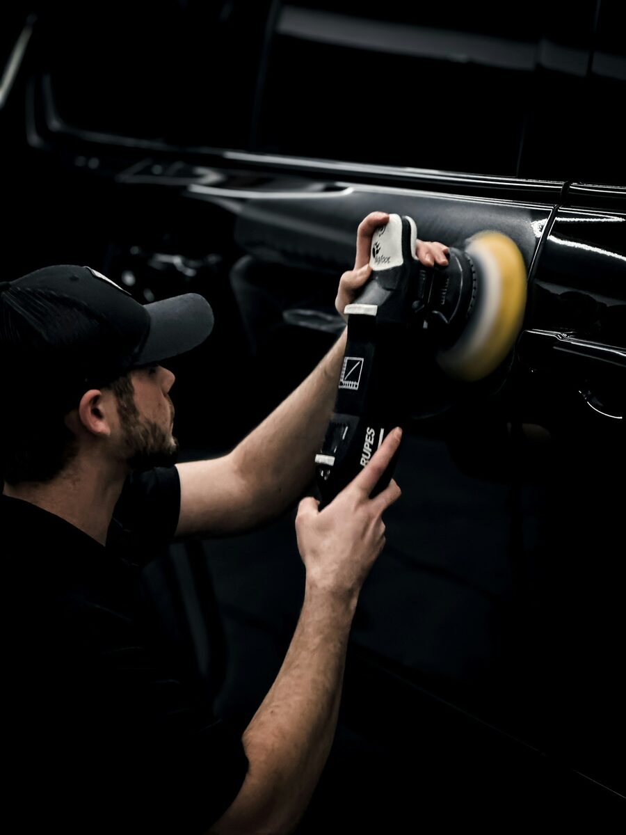 A detailer machine polishing a dark car panel