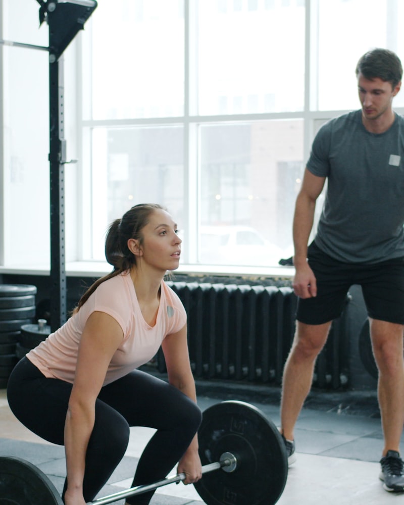A member deadlifting while a coach watches her form