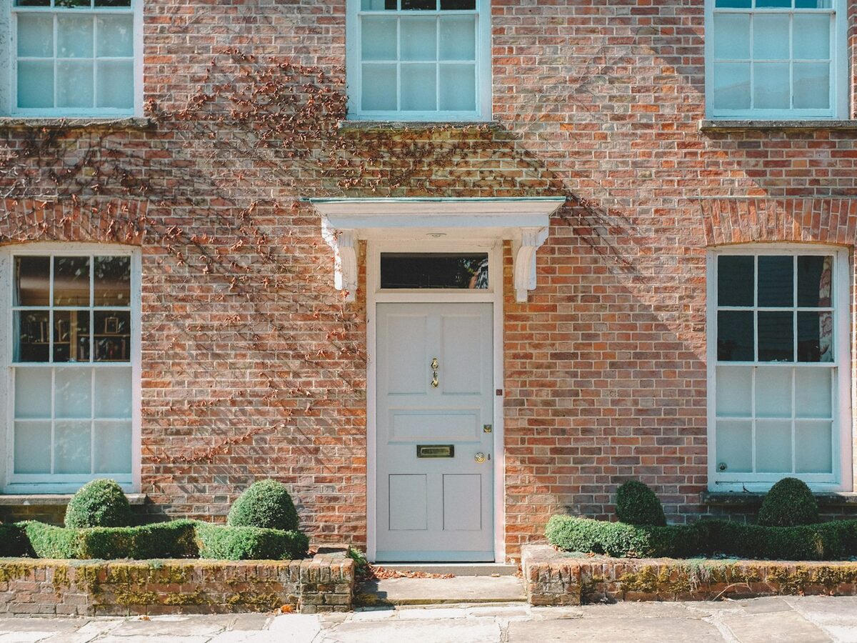 Brick house front with a pale painted door and clipped hedges